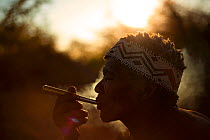 A Zu/'hoasi Bushman smokes a pipe made out of an old artillery cartridge at sunset in the Kalahari, Botswana. April 2012.