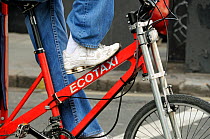 Mans foot resting on the cross bar of an Ecotaxi or Pedicab, Central London, UK
