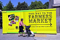 Lady with pushchair looking at direction sign to Islington Farmers Market, London UK