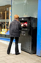 Woman recycling clothes into a clothes bank outside charity shop, Highbury Corner, London Borough of Islington, UK