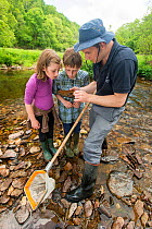 School children looking at rock from the River Haddeom whilst doing invertebrate kick samples, with Westcountry Rivers Trust (WRT) warden. Bury, Exmoor National Park, Somerset, UK. May 2012.