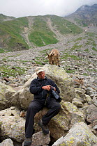 Photographer Patricio Robles Gil reviewing his work with a West Caucasian tur (Capra caucasica) behind him. Kabardino-Balkarsky Nature Reserve, Caucasus Region of Russia.