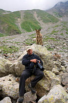 Photographer Patricio Robles Gil reviewing his work with a West Caucasian tur (Capra caucasica) behind him looking on. Kabardino-Balkarsky Nature Reserve, Caucasus Region of Russia.