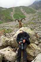Photographer Patricio Robles Gil reviewing his work with a West Caucasian tur (Capra caucasica) behind him. Kabardino-Balkarsky Nature Reserve, Caucasus Region of Russia.