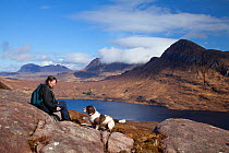 View across Loch Lurgainn to Cul Beag and Cul Mor, with woman hiker and Springer spaniel (Canis familiaris) resting on rocks in the foreground, Ben Mor Coigach Scottish Wildlife Trust reserve, Coigach...