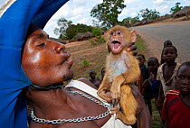 Mozambican man with captive Yellow Baboon youngster (Papio cynocephalus), caught during troop crop raiding, surrounded by children. Pemba to Montepuez highway, north-eastern Mozambique.