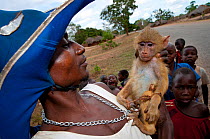 Mozambican man with captive Yellow Baboon youngster (Papio cynocephalus), caught during troop crop raiding, surrounded by children,  Pemba to Montepuez highway, north-eastern Mozambique.
