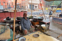 Hindu grain seller for pigeon (Columba livia) feeding for religious purposes, with pigeons being fed in the background, Jodphur, India