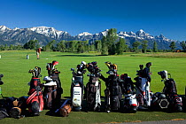 Golf bags and clubs, with golfer, Jackson Hole Golf and Tennis Club, Teton mountain range in the background, Wyoming, USA, July 2011