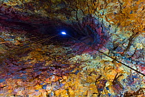 Inside the Thrihnukagigur volcano with torch light of a tour at the end of a tunnel. This dormant volcano is now used for tours, Iceland, June 2012