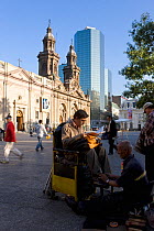 Shoe shining work infront of Cathedral Metropolitana and modern office building in Plaza de Armas, Santiago, Chile, 2008