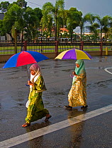 Local muslim woman walking in the rain holding colourful umbrellas, Kota Bharu, Kelantan State, Malaysia 2008