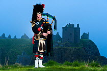 Skirlie McPiper wearing traditional dress playing bagpipes at Dunnotar Castle. Scotland, April 2011.
