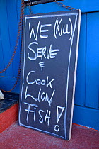 Sign outside Cactus Blue restaurant saying 'We (kill) serve and cook lionfsh!' Lionfish is an invasive species in this region. Kralendijk, Bonaire, Caribbean
