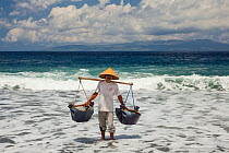 Man collecting black sand in an area which is one of the locations for producing fine restaurant quality salt, most of which is shipped to Japan, Kusimbi Beach, Bali, Indonesia 2009