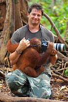 Mark MacEwen, photographer, holding young orangutan (Pongo pygmaeus) investigating camera, Nyaru Menteng Orangutan Reintroduction Project, Central Kalimantan, Borneo, Indonesia, May 2008
