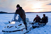 Two divers on a sledge towed by Ski-doo snowmobile to go ice diving, Arctic circle Dive Center, White Sea, Karelia, Northern Russia, March 2010