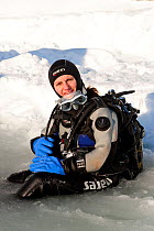 Scuba diver sitting on the maina (sawed triangular entry hole) with melted ice ready to go diving under the ice, Arctic circle Dive Center, White Sea, Karelia, Northern Russia, March 2010