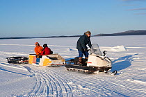 Divers on a sledge towed by Ski-doo snowmobile to go ice diving, Arctic circle Dive Center, White Sea, Karelia, Northern Russia, March 2010
