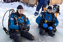 Two Scuba divers at the maina (sawed triangular entry hole) with melted ice ready to go diving under the ice, Arctic circle Dive Center, White Sea, Karelia, Northern Russia, March 2010