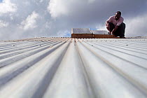Technician fixing solar panel on a corrugated iron rooftop, Miono region, Tanzania.