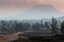 Road built along the path of the latest lava flow, leading towards Nyiragongo volcano silhouetted in the background, Virunga National Park, Democratic Republic of the Congo, August 2010.