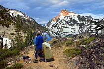 Hiker standing beside tent above Sawtooth Lake with  Mount Regan behind in the Sawtooth Wilderness. Idaho, USA. Model released.