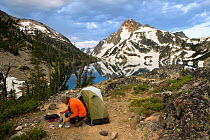 Hiker preparing food next to tent above  Sawtooth Lake with Mount Regan behind, Sawtooth Wilderness, Idaho, USA, July 2011