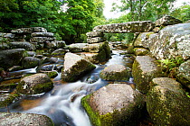 Clapper bridge made from slabs of granite crossing the River Dart at Dartmeet, Dartmoor National Park, Devon, UK.  The bridge probably dates back to medieval times and it has been rebuilt several time...