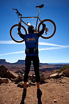 Mountain biker holding up his bike on top of Murphy Climb along the White Rim Road in the Island In The Sky District. Canyonlands National Park, Utah, October 2012. Model released.