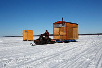 Wooden cabins on sledges are moved into position by skidoo snowmobile, Arctic circle Dive Center, White Sea, Karelia, northern Russia March 2010