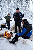 Tourists take lunch break round fire after Dog-sledding inside Riisitunturi National Park, Lapland, Finland