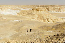 People trekking through chalk rock formations created by sandstorms, White desert, in the Sahara, Egypt, February 2009