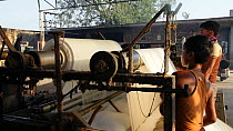 Man and boy feeding undyed fabric into a washing and rolling machine in a sari garment factory, Rajasthan, India, 2011.
