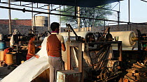 Man and boy feeding undyed fabric into a washing and rolling machine in a sari garment factory, Rajasthan, India, 2011.