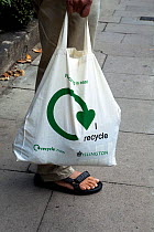 Man holding a reusable cotton shopping bag with &#39;I recycle logo&#39; printed on the side,