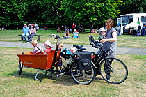 Woman with with bicycle and four small children, two in a workcycles trailer. London Green Fair (previously Camden Green Fair) England, UK, June 2011
