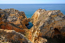 Tourist boat manoeuvering under sandstone rock archway and cliffs.  Ponta da Piedade, Lagos, Algarve, Portugal, June 2012.