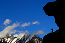 A Balti porter silhouetted standing on a rock, with mountains in the distance, Urdukas Camp (4,000m), Baltoro Glacier, Central Karakoram National Park, Pakistan, July 2007.