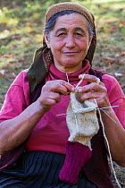 Woman (62 years old) knitting socks from own sheep wool in the garden of her nearby farmhouse in the village of Isverna. Mehedinti Plateau Geopark, Isverna, Romania, October 2012