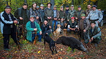 Group of Romanian hunters posing with the only Wild boar (Sus scrofa) shot during a driving hunt in the forest area outside the village of Mehadia, Caras Severin, Romania, October 2012