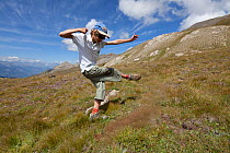 Boy on hillside kicking a fungus, which releases its spores, Queyras, France, August 2011. Model released.