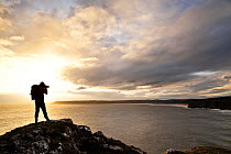 Man taking a photograph of Three Cliffs Bay and Oxwich Bay from above Pobbles Bay, Gower, Swansea, Wales, January 2013. Model released. (This image may be licensed either as rights managed or royalty...