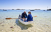 Man and woman rowing a skiff / punt, Par Beach, St. Martin's, Isles of Scilly, Cornwall, England, UK, May 2012. Model released.