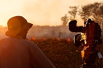 Cameraman Mark Smith filming a grassland fire for the BBC series 'Africa', South Luangwa National Park, Zambia, June 2011.