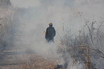 Zambian Wildlife Authority warden standing in the smoke from a grassland fire, South Luangwa National Park, Zambia. June 2011