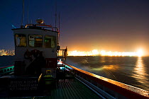 West coast rock lobster (Jasus lalandii) commercial fishing boat (James Archer) leaves the Saldhana Bay harbour before the break of dawn. The lights of the town and the lighthouse flash on the horizon...