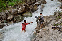 Guides crossing fast flowing river with equipment and bags in Himalayan Brown Bear (Ursus arctos isabellinus) habitat, Dashti Jum Reserve, Tadjikistan, April 2012