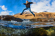 Girl leaps between stepping stones across a mountain river. Akureyri, Iceland. May 2011.