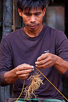 Man tying seaweed onto line, Batasan Island, Danajon Bank, Central Visayas, Philippines, April 2013